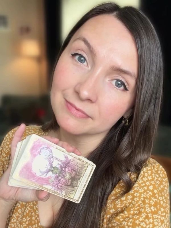Woman holding tarot cards and smiling gently.