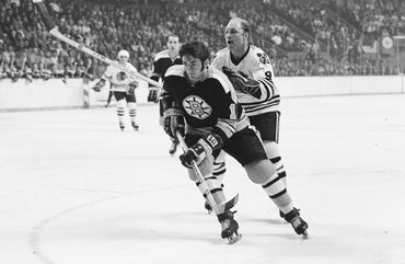 Bobby Hull letting the Bruins player know that he is coming for the puck.