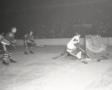 Pierre Pilote and Bobby Hull #16 skate to the net as the goalie freezes the puck vs the Red Wings