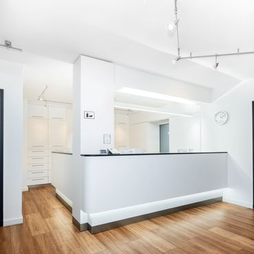 Modern, minimalist white reception area with wooden flooring and bright lighting.
