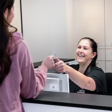 A receptionist happily hands a card to a visitor at the front desk.