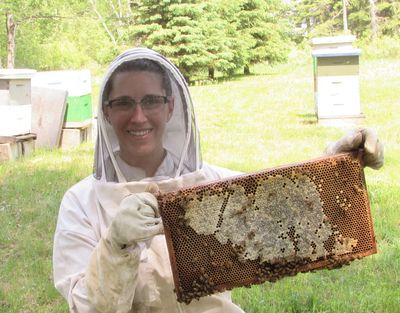 Juliette wearing a full beekeeping suit holding a beehive frame