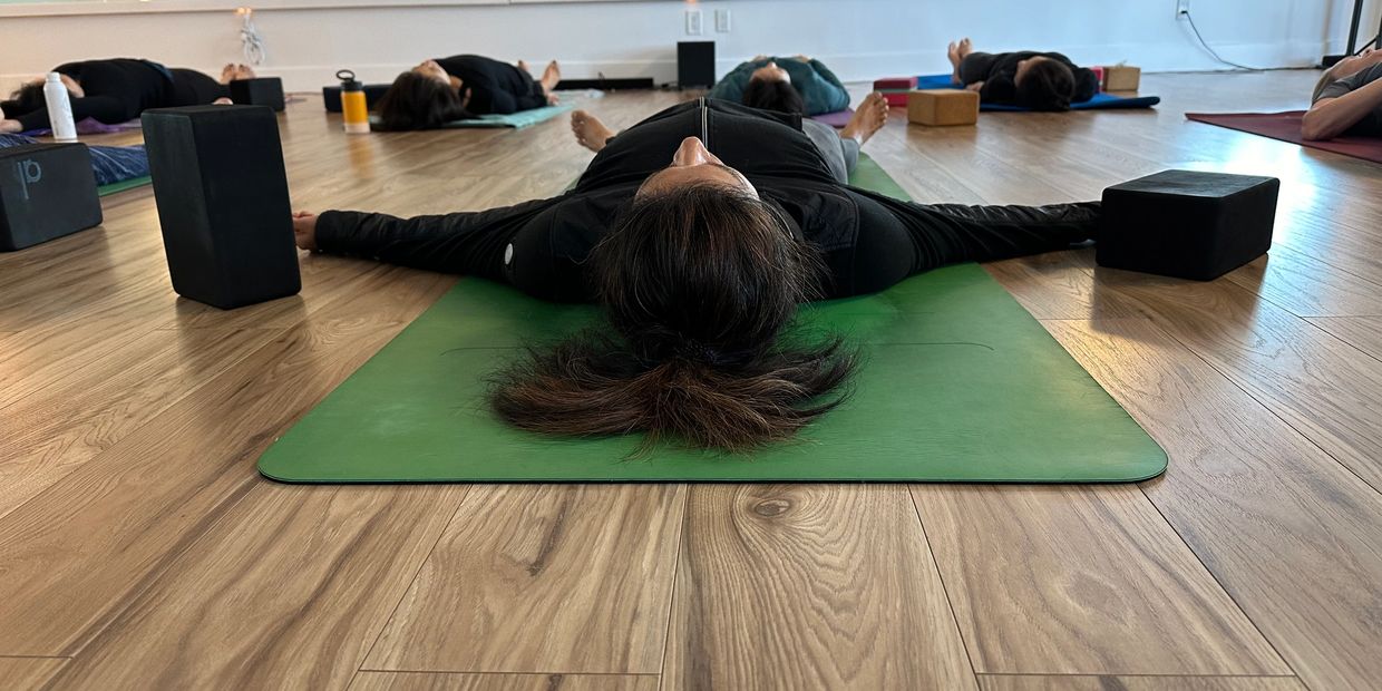 People resting on mats in a yoga class with blocks beside them.