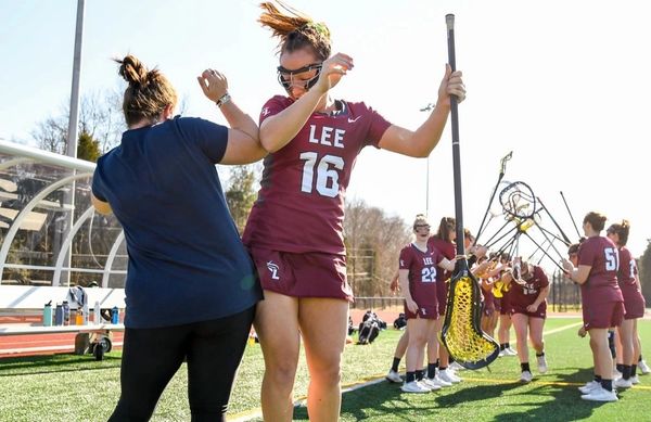 Female lacrosse player celebrating with coach on field.