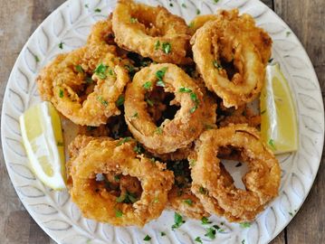 Plate of golden-brown fried calamari rings garnished with herbs and lemon wedges.