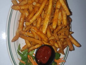 Plate of crispy seasoned French fries with ketchup and garnish.