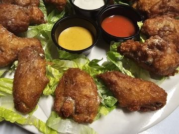 Plate of fried chicken wings with three dipping sauces on lettuce.