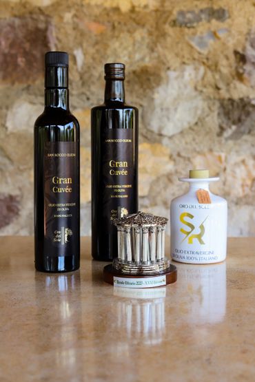 Two bottles and one ceramic container of Italian extra virgin olive oil with a trophy on a marble surface.