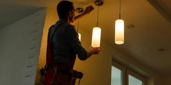 A man installing a hanging pendant light in a dimly lit room.