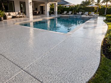 Modern backyard pool with polished concrete deck and lounge chairs under umbrellas.
