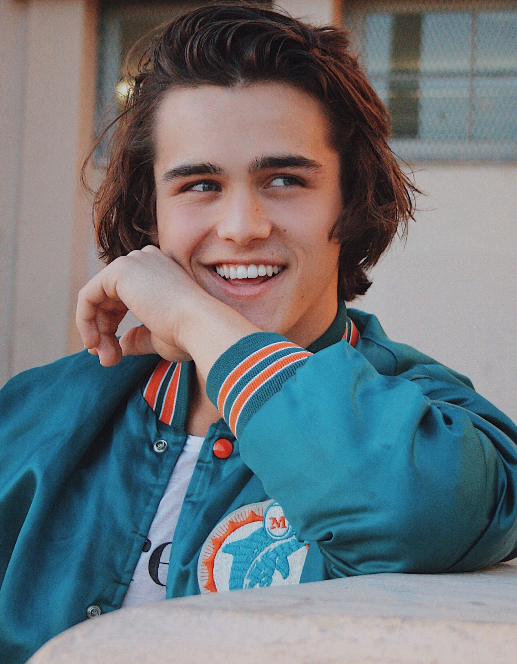Smiling young man in a blue jacket resting his arm and looking away.