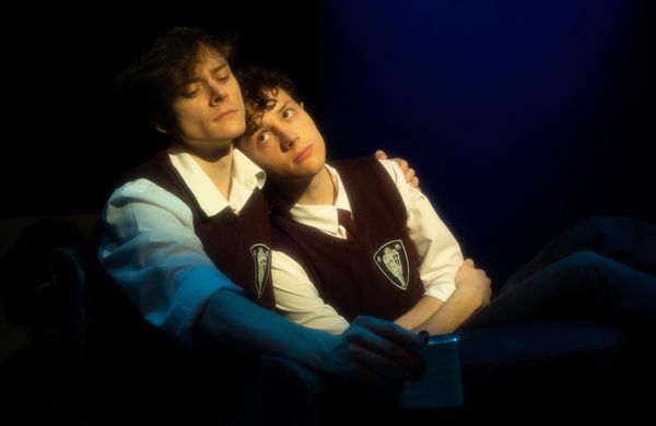 Two people in school uniforms embracing in a dimly lit setting.