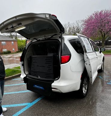 White BraunAbility van with open rear and side doors in a rainy parking lot.