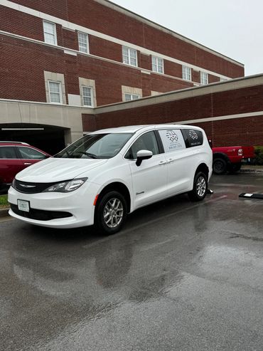 White Chrysler Pacifica van parked in front of a red brick building on a rainy day.