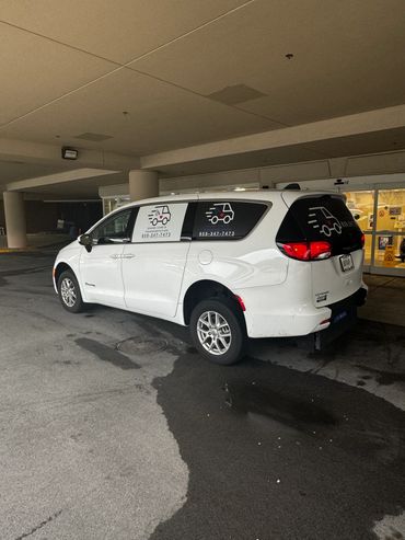 White van with OANA Care & Transportation logo parked near a building entrance.