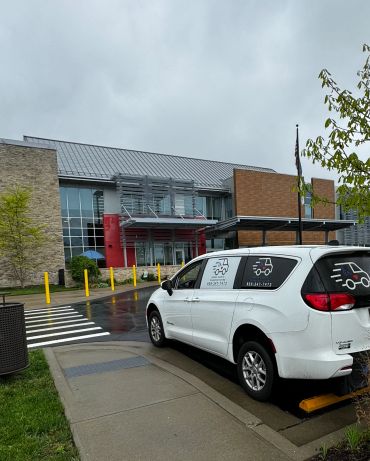 White van parked outside a modern building on a rainy day.