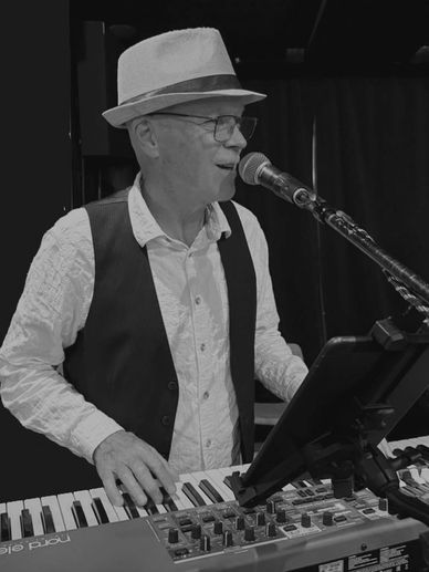 Elderly man in a hat singing and playing keyboard.
