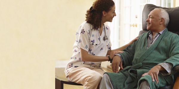 Caregiver talks with elderly man in green robe.