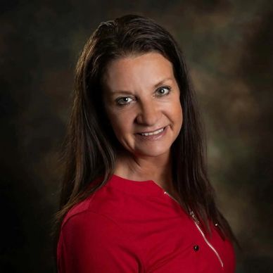 Woman with long dark hair smiling against a dark background.
