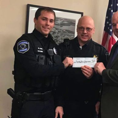 Two police officers and a man holding a certificate or check indoors.