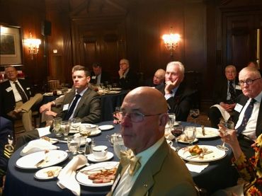 A formal dinner with men in suits seated around tables in a dimly lit room.