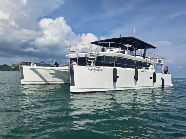 Two white catamarans named Eagle Magic 2 sailing on calm waters under a partly cloudy sky.
