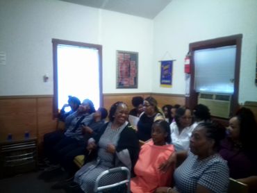 A group of women and children sitting closely in a small room with wooden walls.