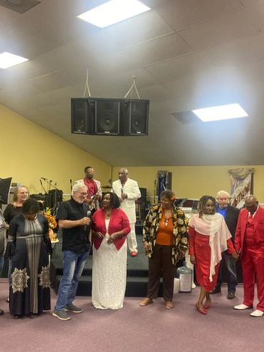 Group of people standing together inside a room, some on a stage.