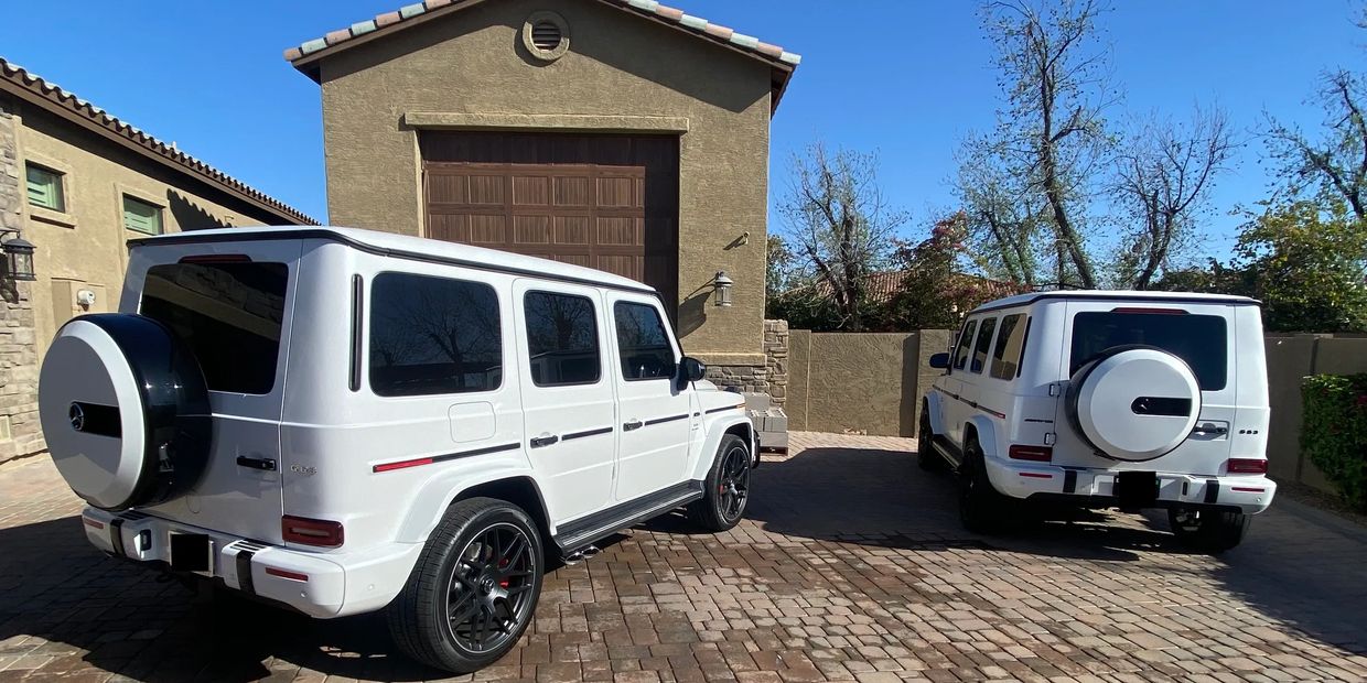 Two white Mercedes G-Class SUVs parked in a driveway on a sunny day.