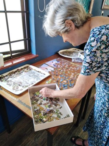 Elderly woman focused on assembling a jigsaw puzzle on a wooden table.