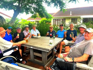 A group of elderly men enjoying drinks outdoors around a wooden table.
