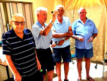 Four elderly men playing darts indoors, enjoying leisure time.