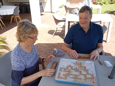 Two elderly people playing Scrabble outdoors on a sunny day.