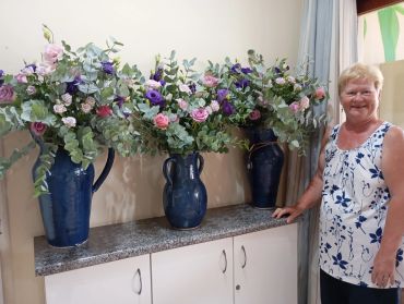 Woman smiling next to three blue vases filled with colorful flowers.