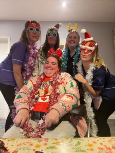 A group of five people dressed in festive Christmas accessories smiling.