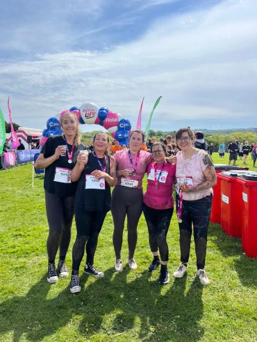 Five women celebrating after a race event outdoors on a sunny day.