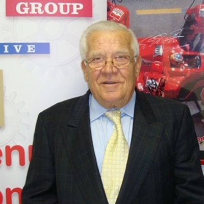 Elderly man in suit and tie smiling.