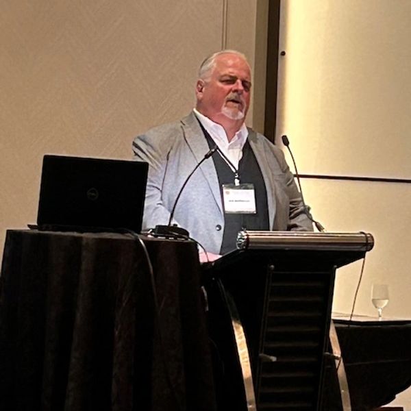 Man speaking at a podium with laptop nearby.