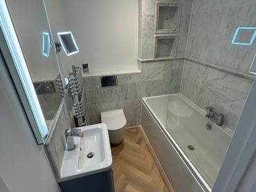 small bathroom, white floating toilet & basin, chrome radiator/fittings grey wall tiles, mirror