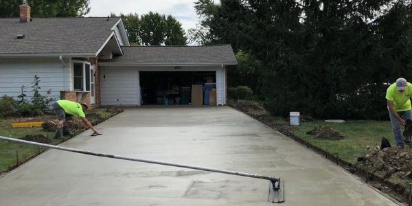 Workers smoothing freshly poured concrete driveway in front of a house.