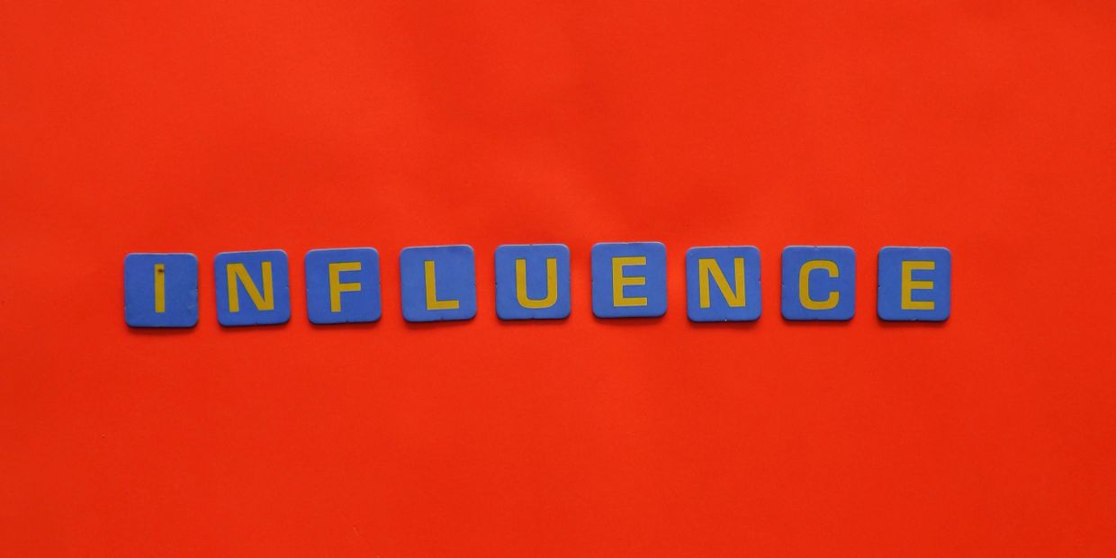 Blue tiles spell out 'INFLUENCE' on a bright red background.