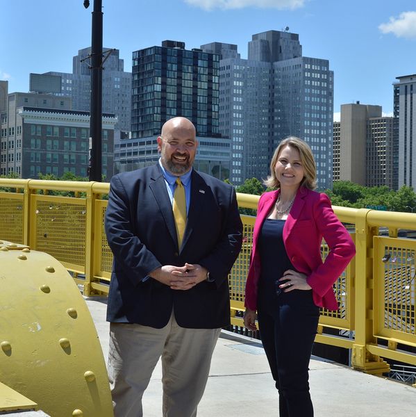 Two professionals smiling on a yellow city bridge with skyscrapers behind them.