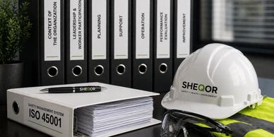 ISO 45001 safety management system binder with protective gear on a desk.