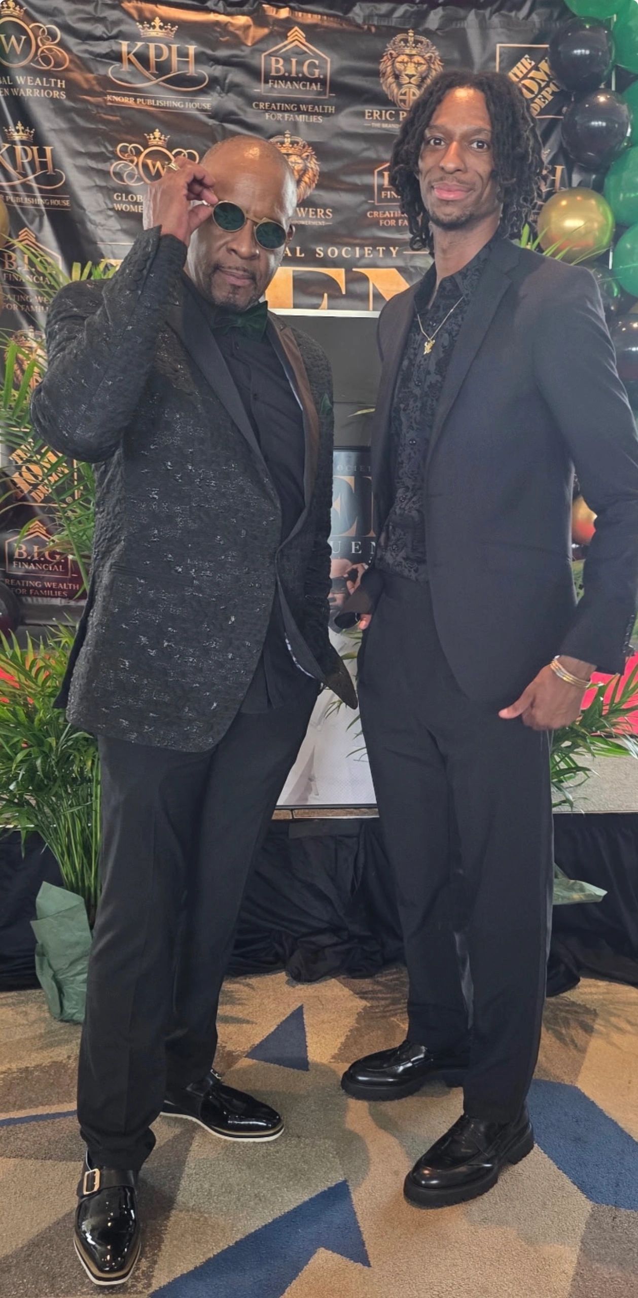 Two men in black suits posing confidently at a formal event.