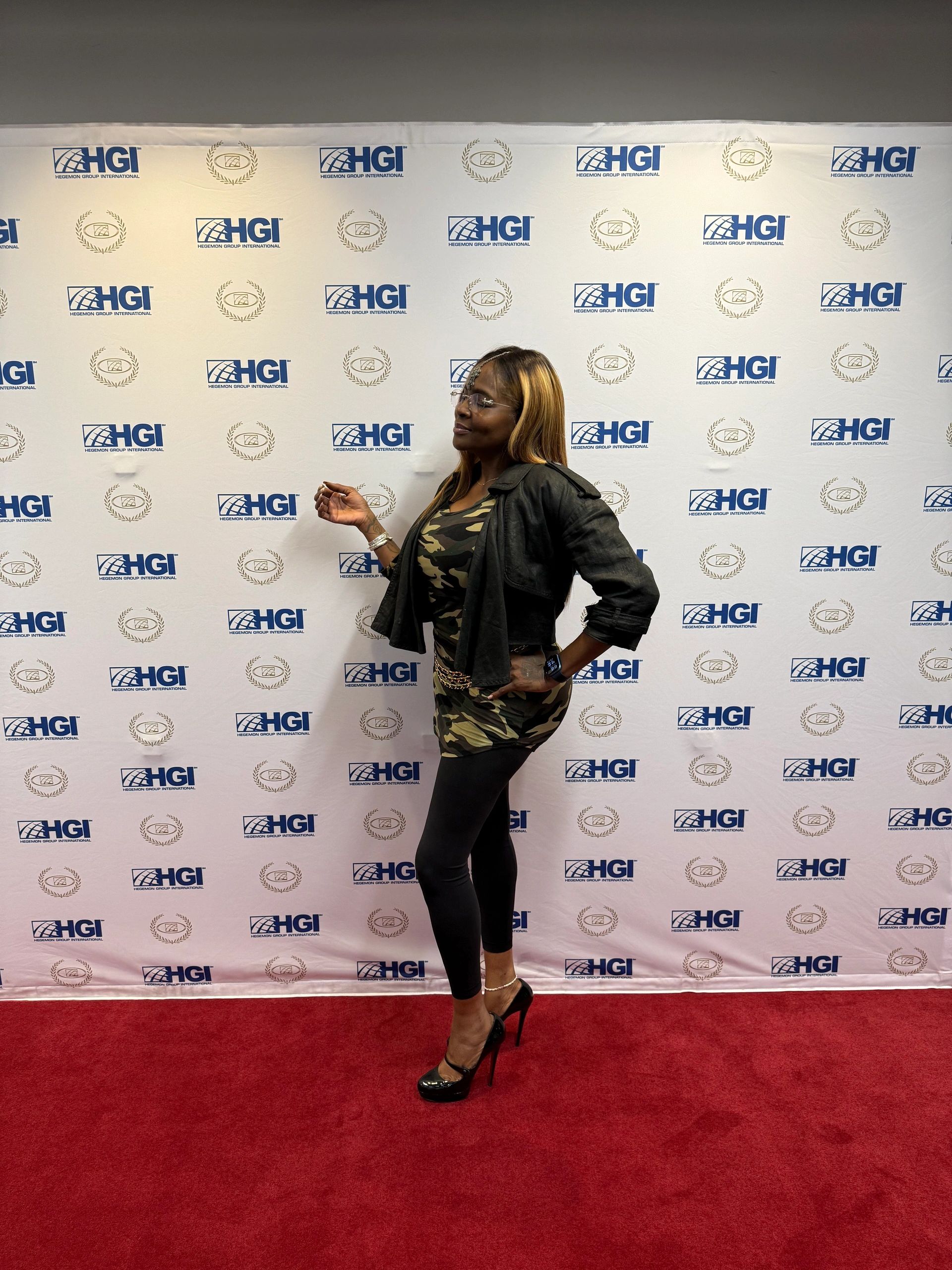 Woman posing on a red carpet with a branded backdrop.