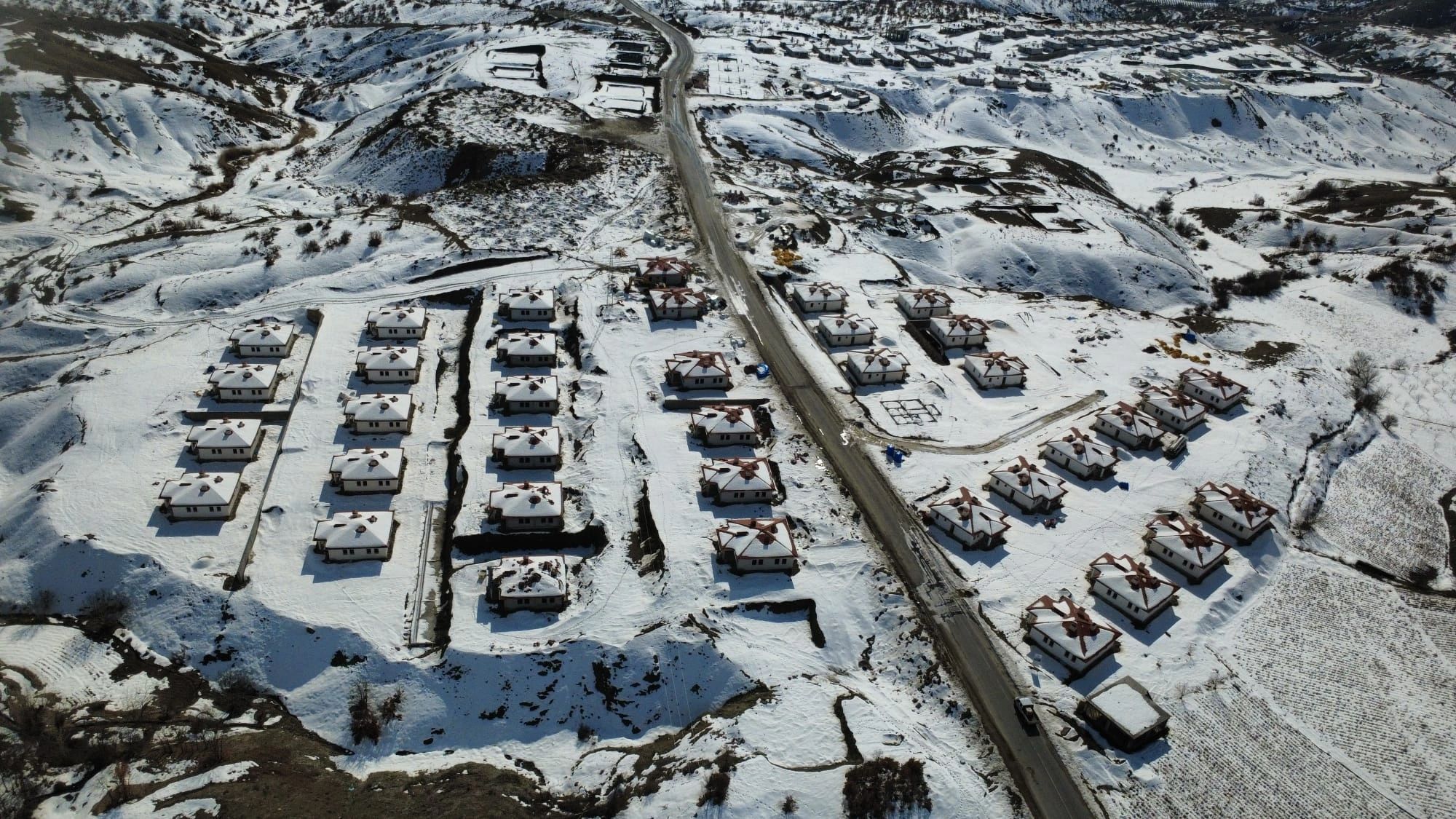 A snowy village with houses arranged along a road in a mountainous area.