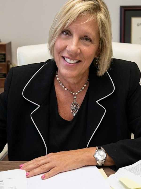 Smiling woman in black blazer sitting at desk with documents.