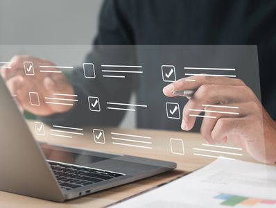 Person with a pen interacting with a digital checklist overlay, next to a laptop.