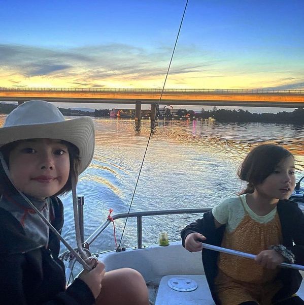 Children steer a boat with Commonwealth Avenue Bridge and the National Museum of Australia  at dusk