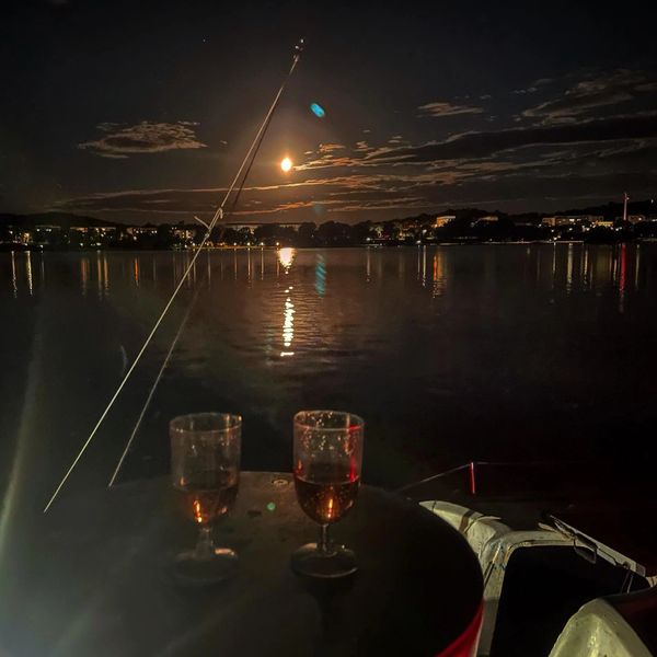 Two glasses of wine sit on a dock overlooking a brilliant moon rise over Lake Burley Griffin